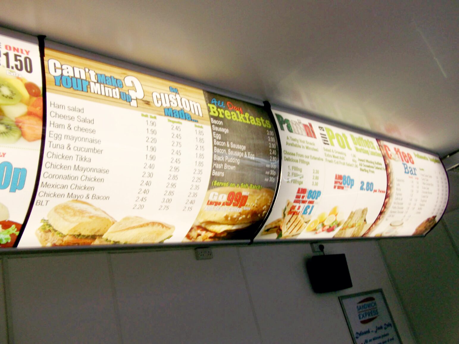 Curved illuminated sandwich and breakfast menu panels mounted at ceiling height