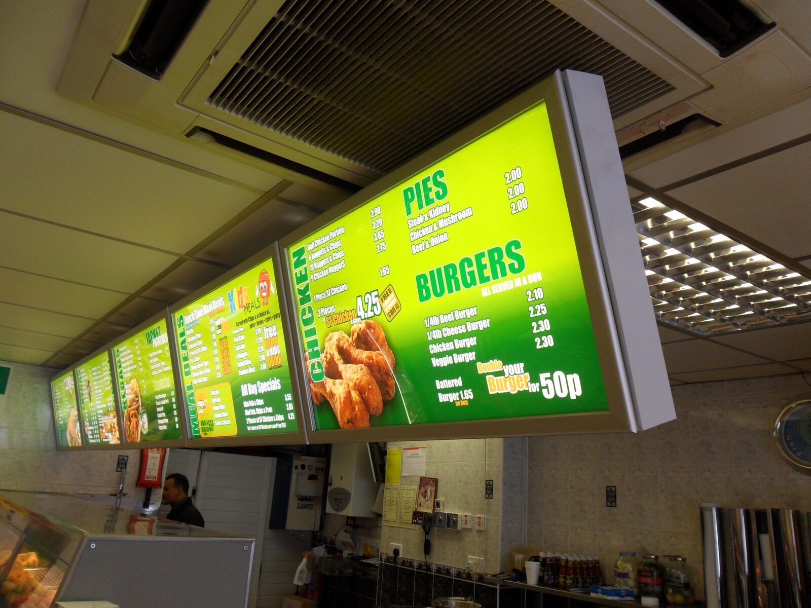 Green illuminated menu boxes running the length of a fish and chip shop counter