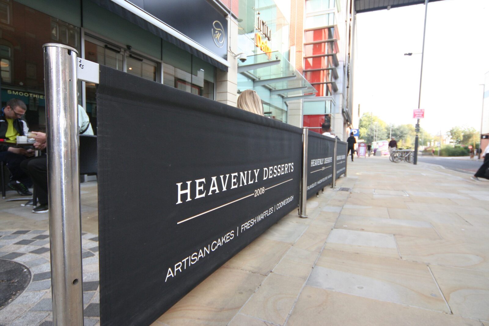 Heavenly Desserts branded café barrier along a pavement seating area