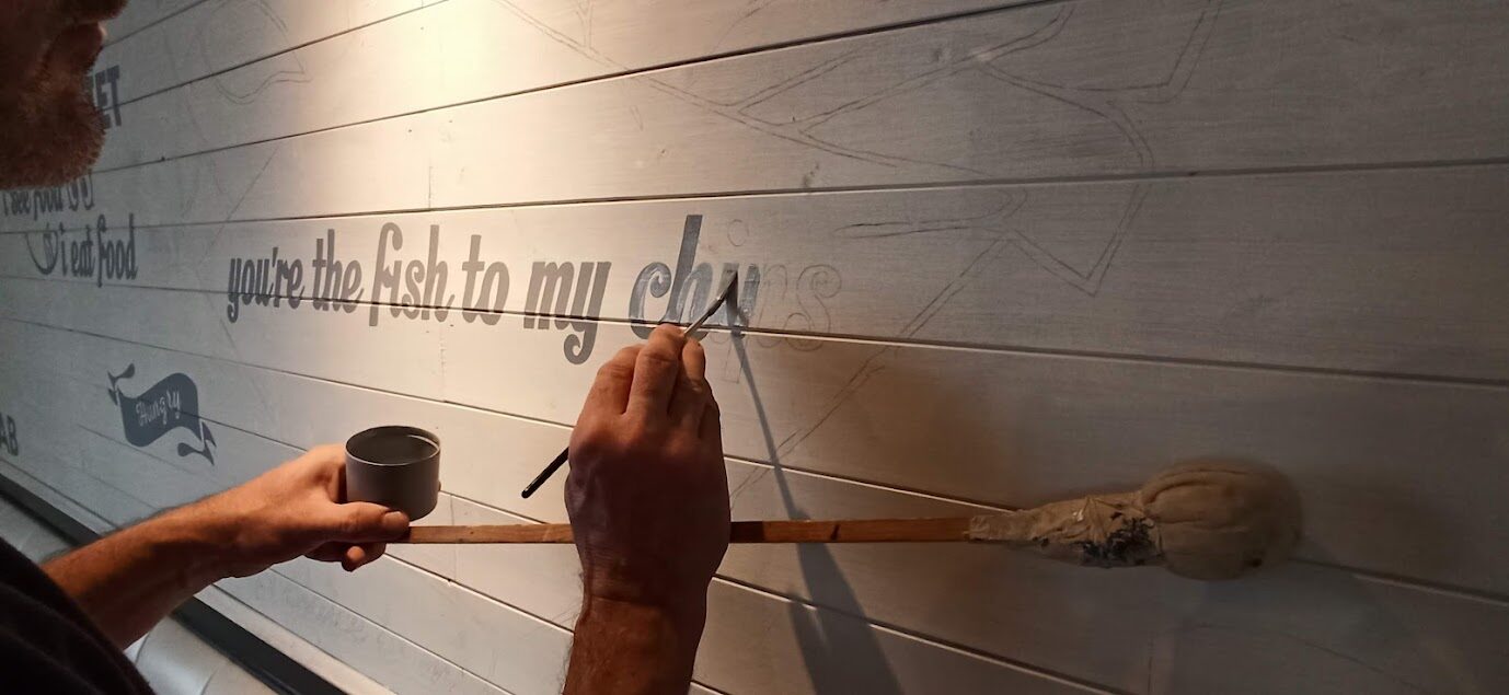 Sign writer hand-painting lettering onto timber